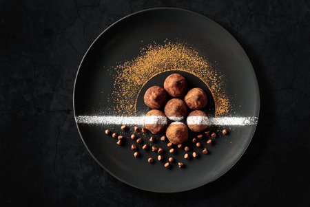 Chocolate truffles on a black plate. Sweets are sprinkled with cocoa powder. Black plate with...