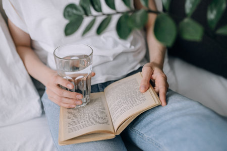 Young woman reading a book and holding a glass of water close-upの写真素材