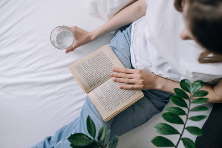 A young woman in casual clothes spends time reading a book and holding a glass of water top viewの写真素材