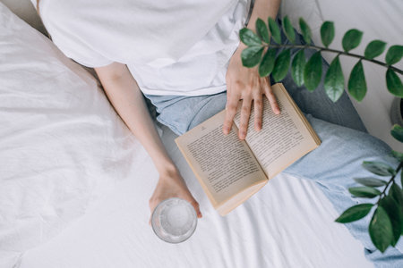 Young woman in casual clothes reads a book and holds a glass of water top viewの写真素材