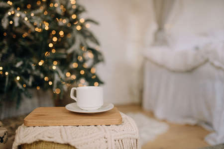 Cup of coffee on a stand in the bedroom on the background of the bed and Christmas treeの写真素材