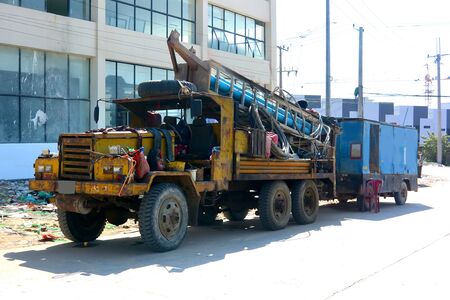 Old yellow drilling machine drags a blue trailer, Cambodia