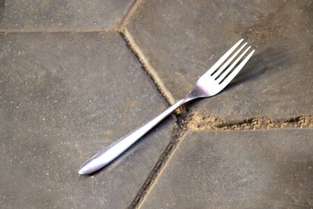 A metal fork lies on a concrete floor