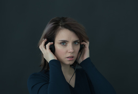 portrait of young beautiful girl in studio in studio with headphones on a dark backgroundの写真素材