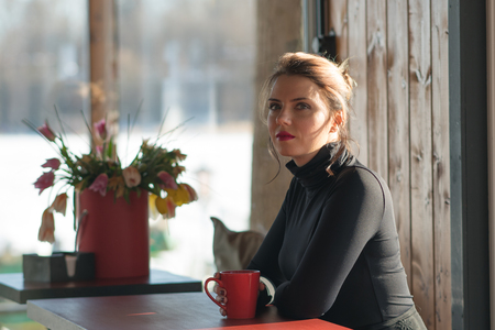 young beautiful girl sits in a cafe with a red cup of coffeeの写真素材