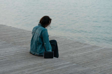 young beautiful woman sits on a wooden bridge near the lakeの写真素材