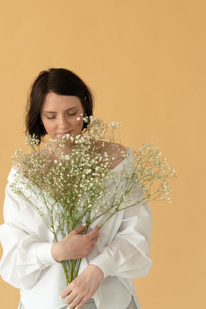 portrait of a young beautiful woman in the studio with white flowers on a yellow backgroundの写真素材
