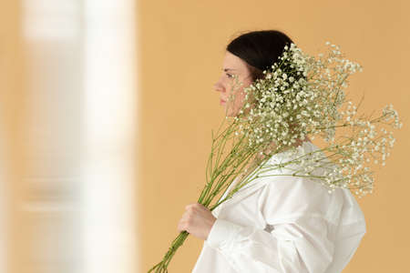 portrait of a young beautiful woman in the studio with white flowers on a yellow backgroundの写真素材