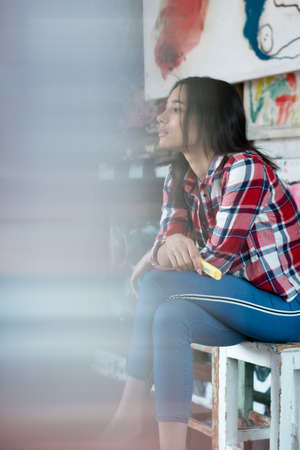 young pretty woman pose in the studio, sitting on a chair in a red shirtの写真素材