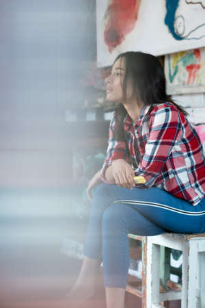 young pretty woman pose in the studio, sitting on a chair in a red shirtの写真素材