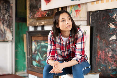 young beautiful woman posing in a red shirt in the studio, sitting on a white chairの写真素材