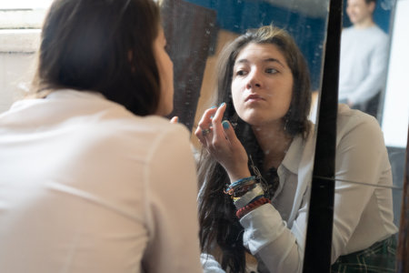Young woman looking in the mirror and applying makeup on her face.の写真素材