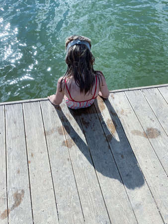 a little girl in a striped swimsuit stands on a wooden bridgeの写真素材