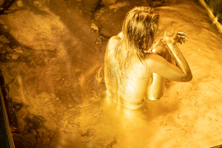 Young woman taking a bath in a hot tub with golden water.の写真素材