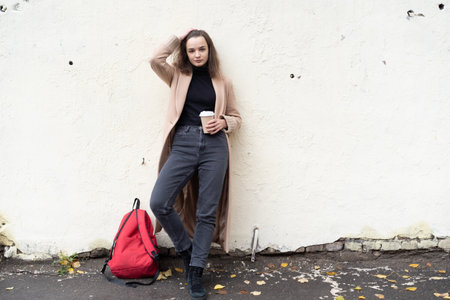 Beautiful young woman with a red backpack and coffee cup on the streetの写真素材