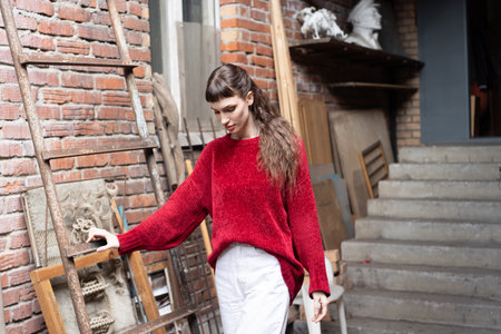 Young beautiful woman in a red sweater and white pants in the interior of the houseの写真素材