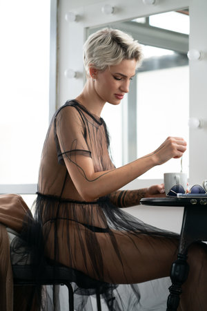 beautiful blonde woman in black dress sitting at table with cup of coffeeの写真素材