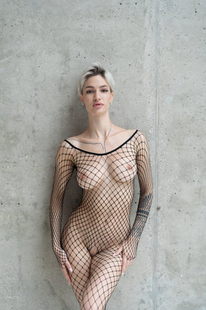 young beautiful girl posing nude in studio, standing in fishnet stockingsの写真素材