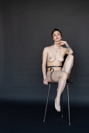 young beautiful girl posing nude in the studio, sitting on a chairの写真素材