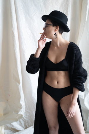 Beautiful sexy lady in elegant black clothes and hat posing in the studioの写真素材