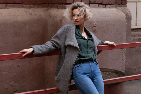 Portrait of a beautiful blonde girl with curly hair in a gray coat and blue jeans on the streetの写真素材
