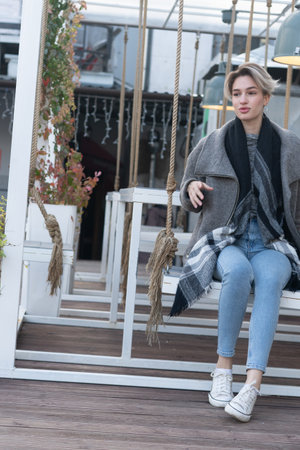Young woman sitting on a swing in the park, wearing a coat and jeansの写真素材