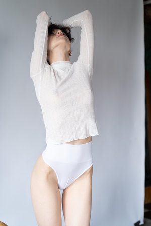 young beautiful girl posing in studio, standing in a white sweater and underwearの写真素材