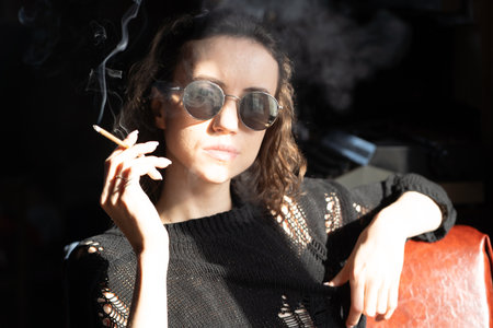 Portrait of a beautiful young woman in sunglasses smoking a cigarette.の写真素材