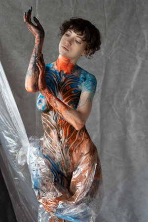 young beautiful girl posing nude in studio, covered with colored layers of paintの写真素材