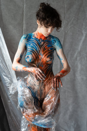 young beautiful girl posing nude in studio, covered with multicolored paintの写真素材