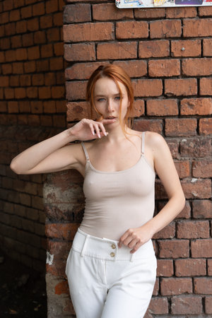 Portrait of a beautiful young redhead woman in a beige top and white pants.の写真素材