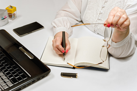 Close-up of female hands with laptop computer, smartphone and office tools on tableの写真素材