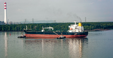 Tugboats tugs help turn around a large oil tanker on the way out of the harborの写真素材