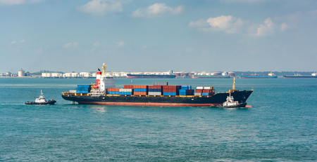 Tugboats tugs help turn around a large container ship on the way out of the harborの写真素材