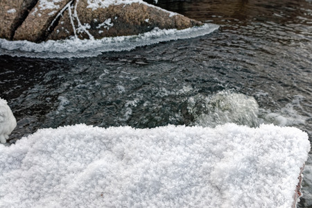 Mountain stream running covered by snow in winter with some stones in waterの写真素材