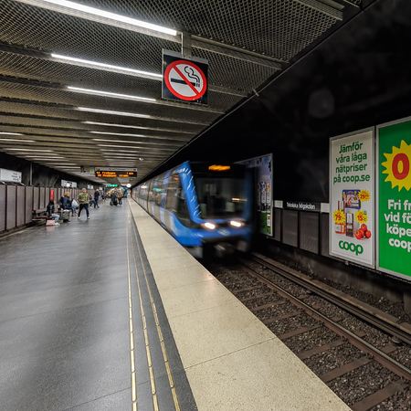 A blue subway train arrives at the platform at the station in the Stockholm metro system where a man waiting for the train.のeditorial素材