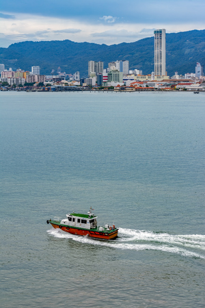 PENANG, MALAYSIA - January 02, 2017: Orange and white pilot boat arrives to collect pilot from ship at Malacca Strait water next to George Town on the opposite shore.のeditorial素材