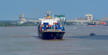 Container vessel sails down the Song Long River from Ho Chi Minh City in front of powdered cement...