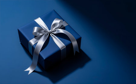 Blue gift box with a silver bow on a blue background with copy spaceの素材