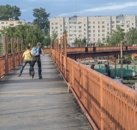 Two young boys riding on roller skates on a long wrap bridge over railroad tracks at the train station.の写真素材