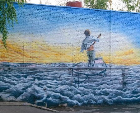 Picture on a brick wall, depicting a boy standing with a paddle boat, floating on the waves to the solar horizonのeditorial素材