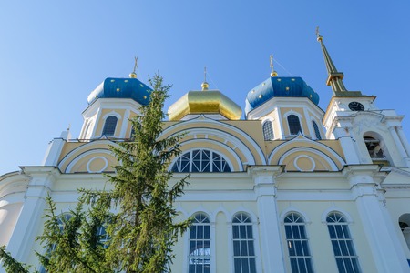 Wall and upper part of church with three blue and gold domes and bell tower against blue cloudless...