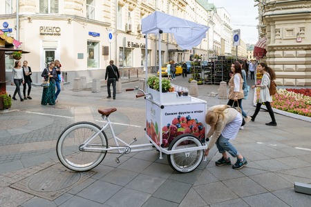 Moscow, Russia - July 07, 2016: Girl sets the counter with a refrigerator, attached to the bike, for sale of fresh fruits and berriesのeditorial素材