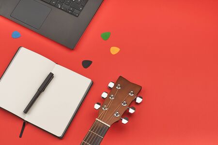 Online guitar learning concept with laptop, notebook and guitar on red backgrond. Minimal flat lay viewの写真素材