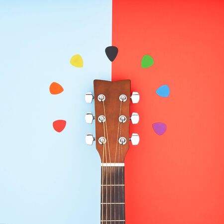 Colorful picks around acoustic guitars headstock. Flat lay on light blue and red backgroundの写真素材