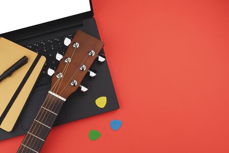 Online guitar learning concept with laptop, notebook and guitar on red backgrond. Minimal flat lay viewの写真素材