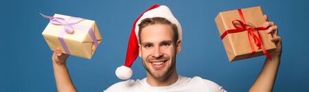 happy young man in santa hat holding presents isolated on blueの写真素材