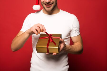 cropped view of smiling young man in santa hat holding present isolatedの写真素材