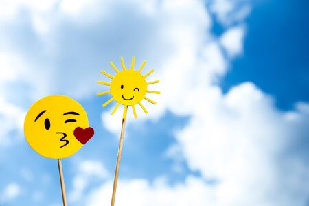 KYIV, UKRAINE - MAY 25, 2019: paper cut blowing kiss emoji and smiling sun on blue sky background with cloudsのeditorial素材