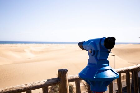 selective focus of binoculars and sand hills near Atlantic ocean against clear blue sky at sunny day in Maspalomas, Gran Canariaの写真素材